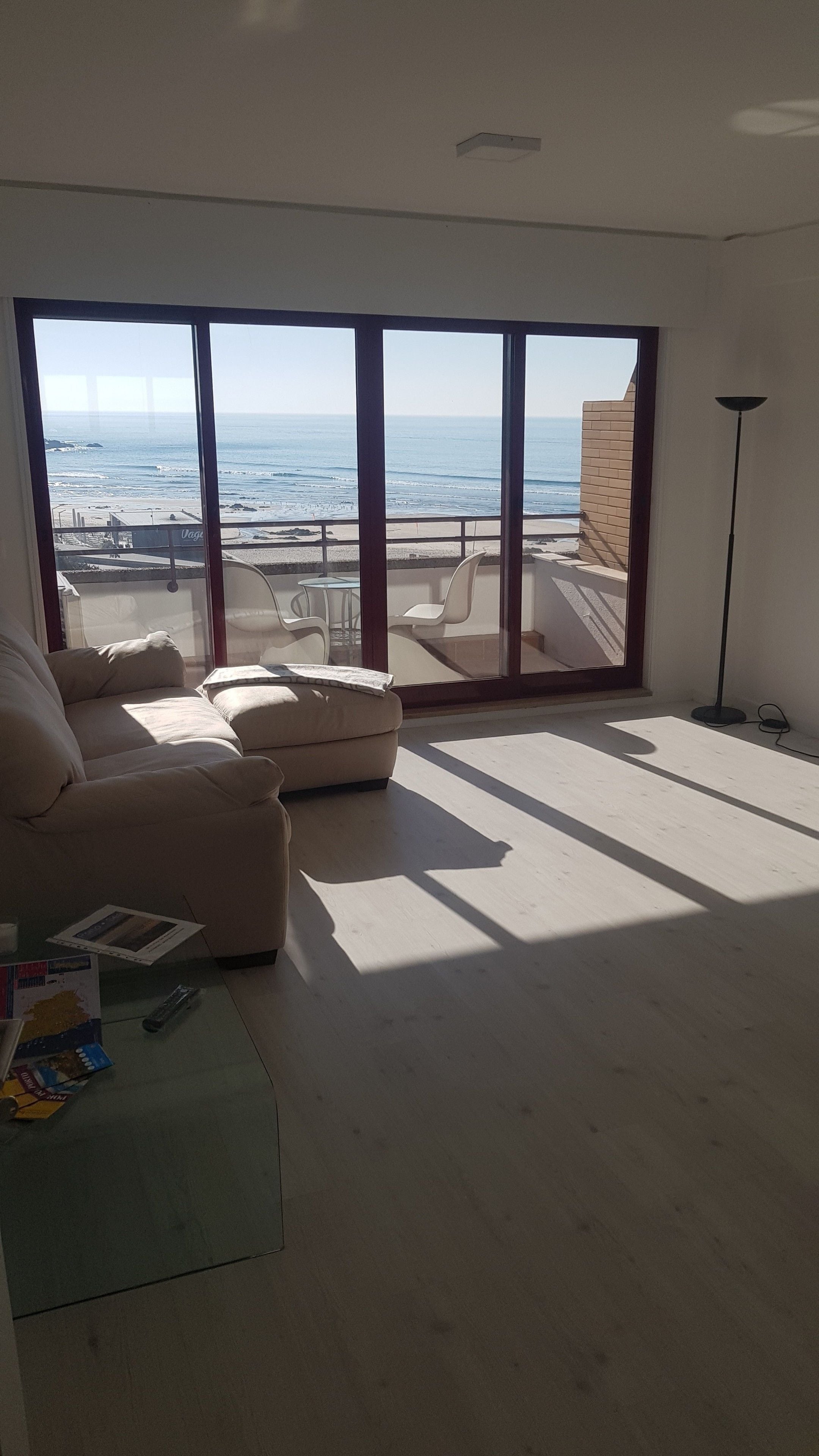 A spacious living room with a large sliding glass door leading to a balcony with a view of the ocean.