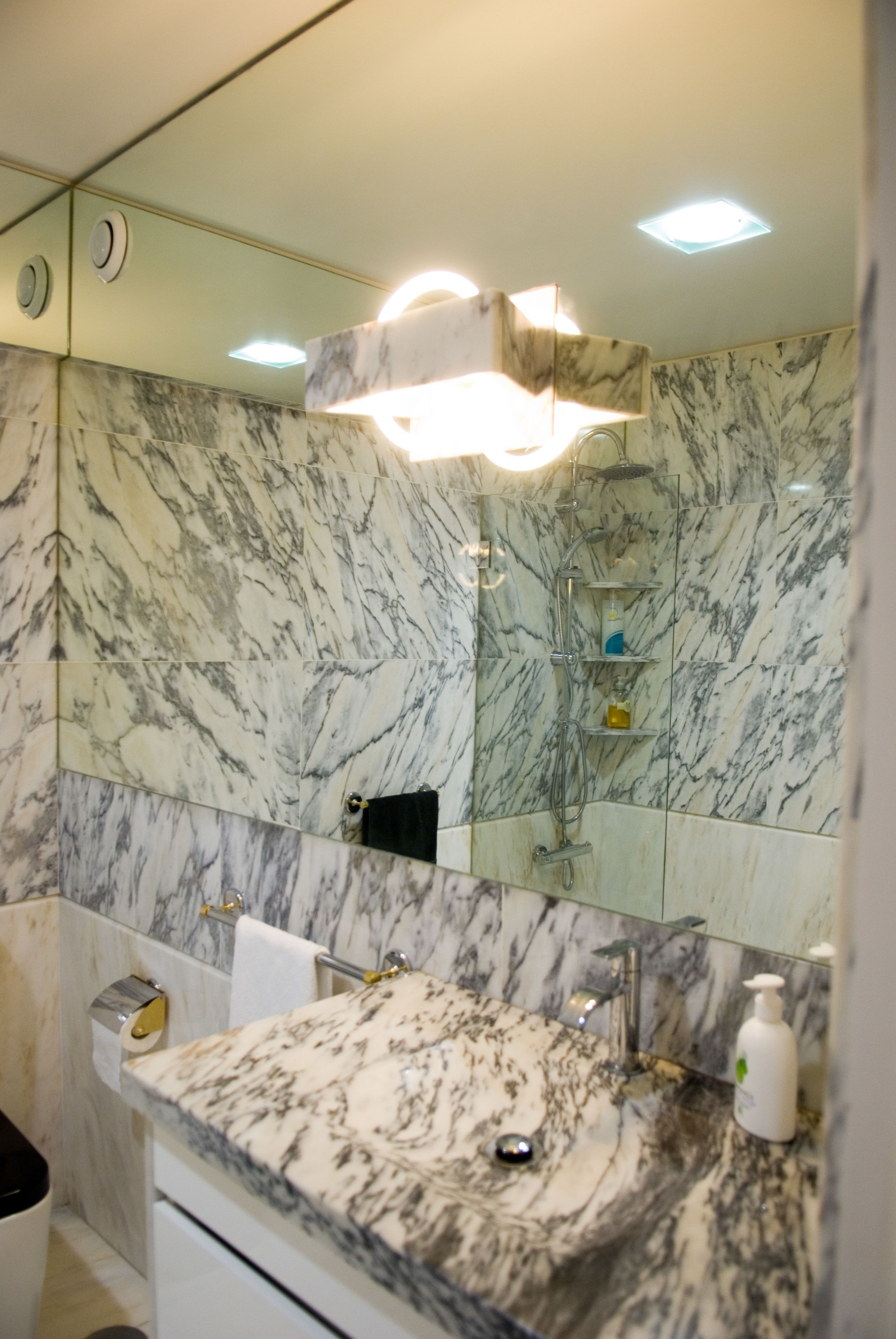 Une salle de bain avec un lavabo en marbre, un miroir, une douche et des toilettes.
