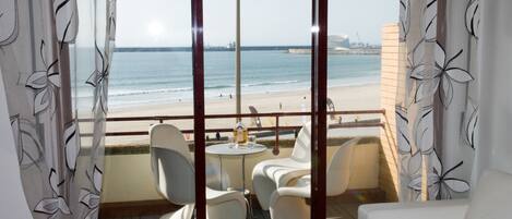 A balcony with a view of the beach, white chairs, a small round table, and a sofa.