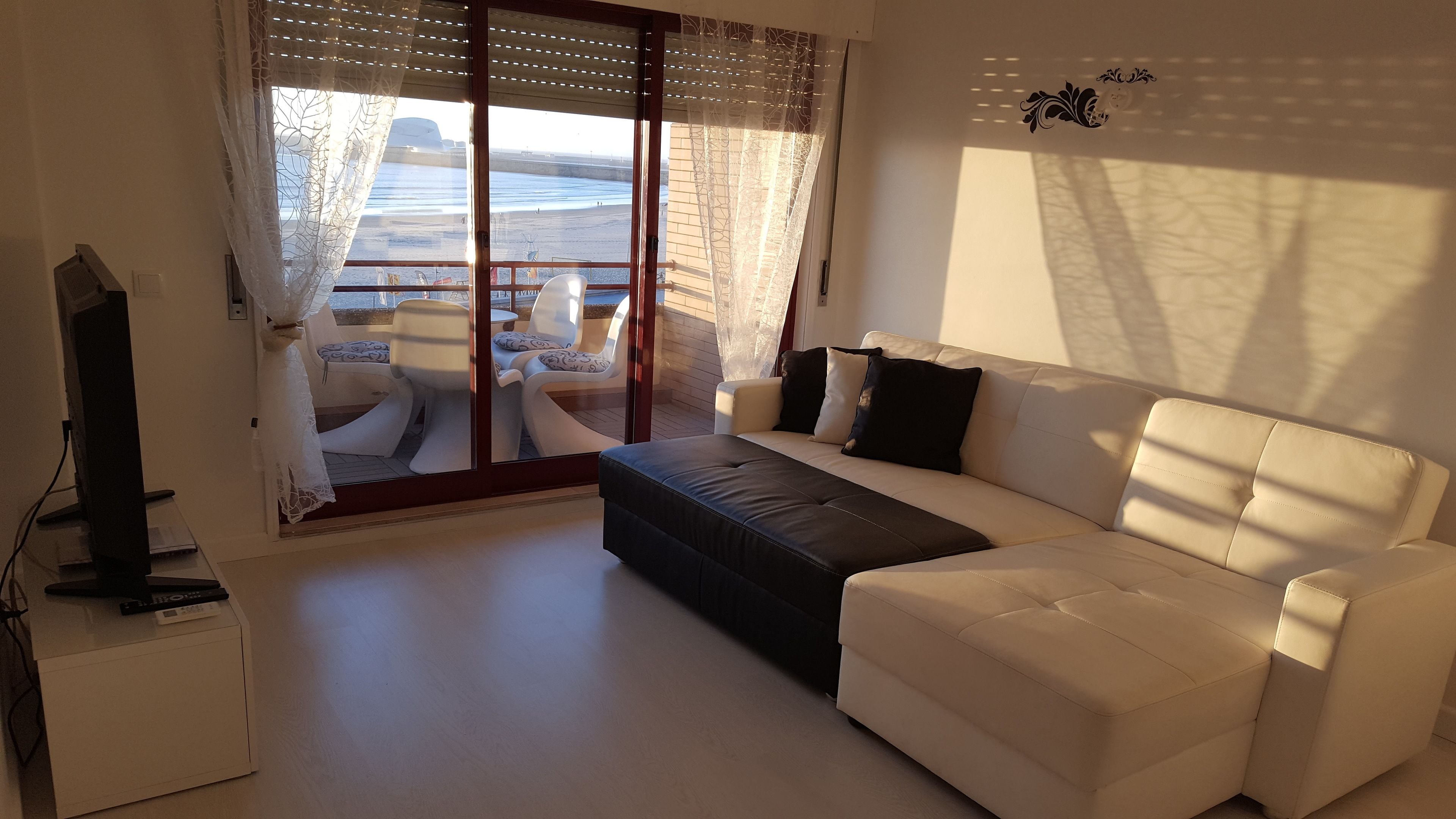A living room with a sofa, a TV, and a view of the beach through a glass door.