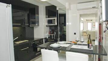 A modern kitchen with black and white cabinetry, a microwave, and a dining area with two white chairs and a table set for two.