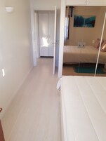 Un dormitorio con cama, mesita de noche, un cuadro en la pared y una puerta que da a otra habitación.
