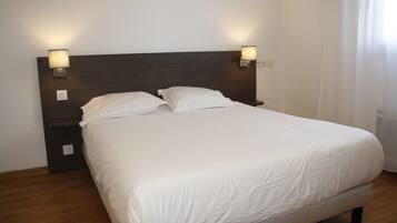 A neatly made bed with white linens, two bedside lamps, and a dark wooden headboard.