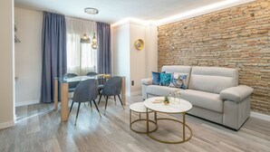 Een moderne woonkamer met een stenen muur, een beige bank, een glazen eettafel en een ronde salontafel.