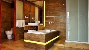 Een moderne badkamer met een houten wastafelmeubel, een ruime badkuip, een glazen douchecabine en een toilet.