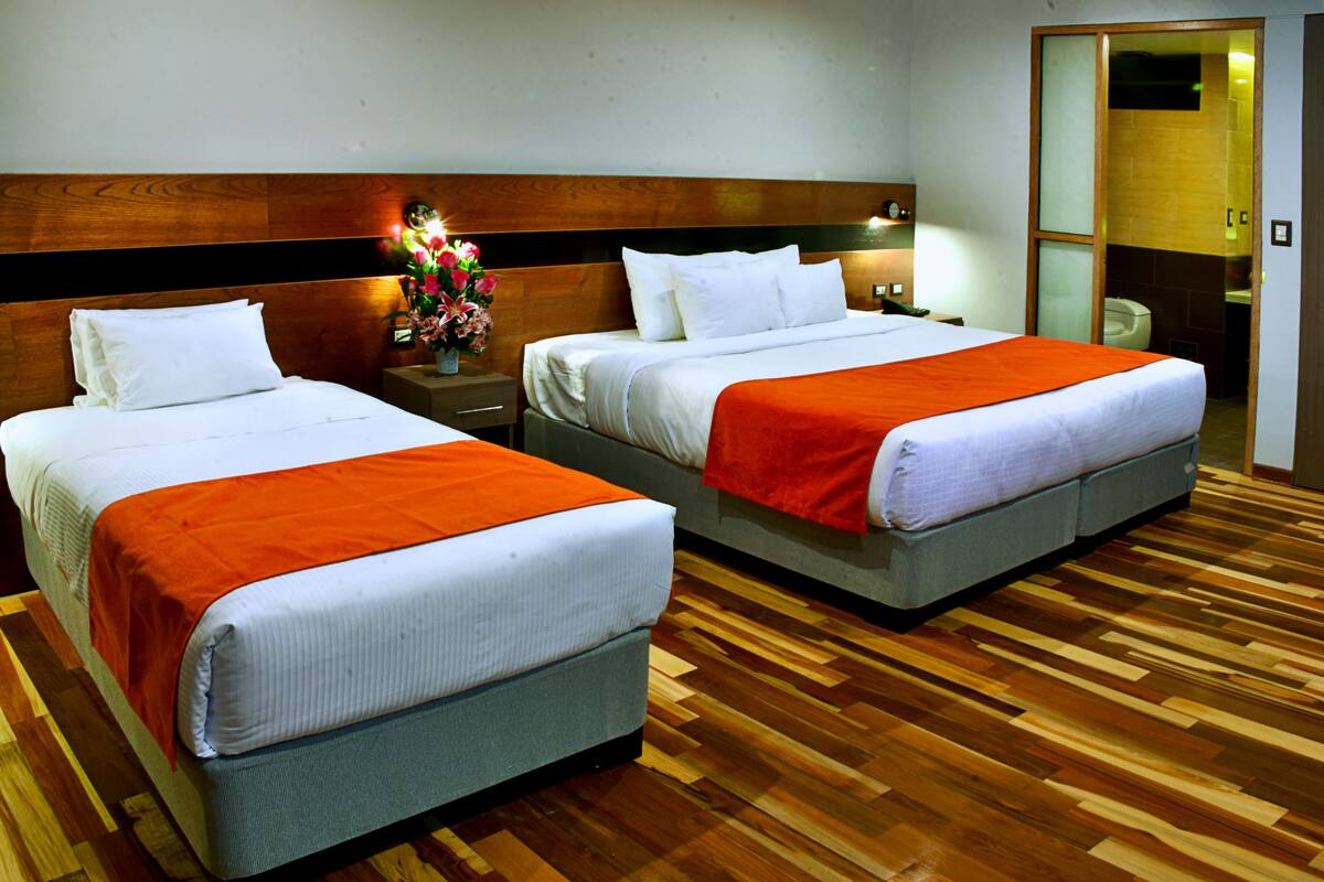 A hotel room with two beds, wooden flooring, and a nightstand with a vase of flowers.