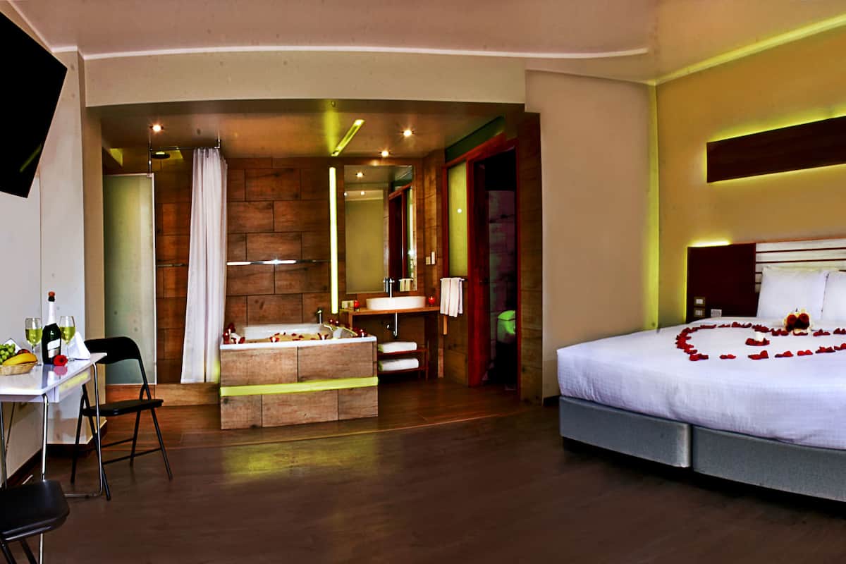 A hotel room with a large bed, a desk with a chair, a small bathroom, and a mirror.