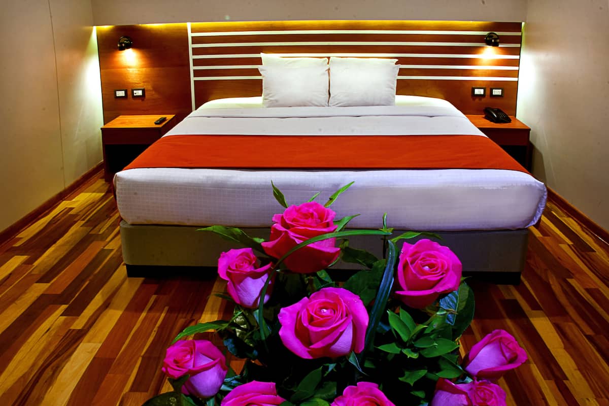 A hotel room with a large bed, wooden headboard, bedside tables, and a vase of pink roses.