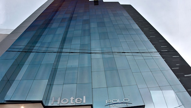 Een moderne hotelentree met een glazen gevel, een zichtbare trap naar de lobby en de naam van het hotel, "Hotel Polo Corporate", duidelijk in het zicht.