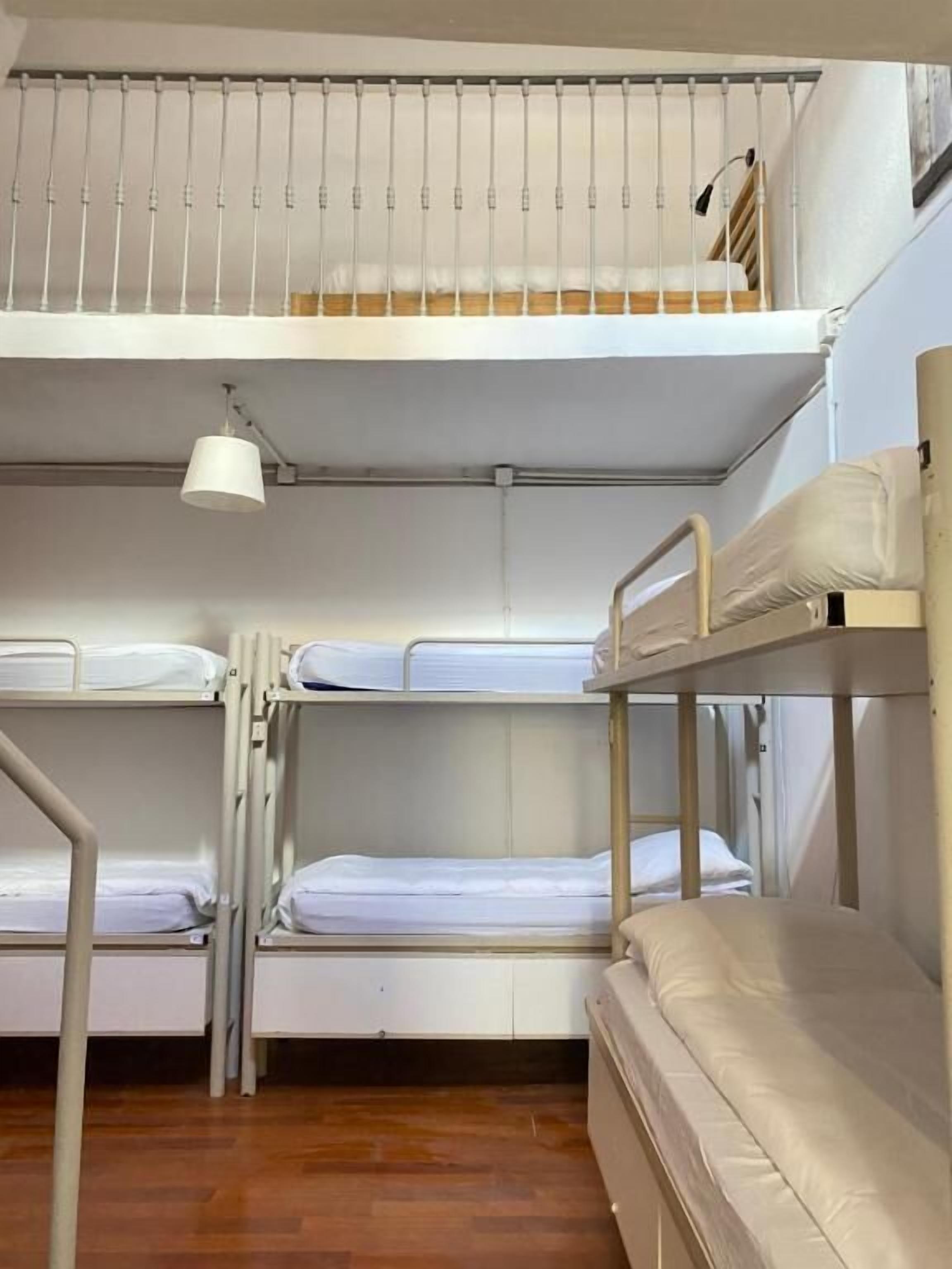 A bunk bed room with a ceiling fan, wooden flooring, and a window with blinds.