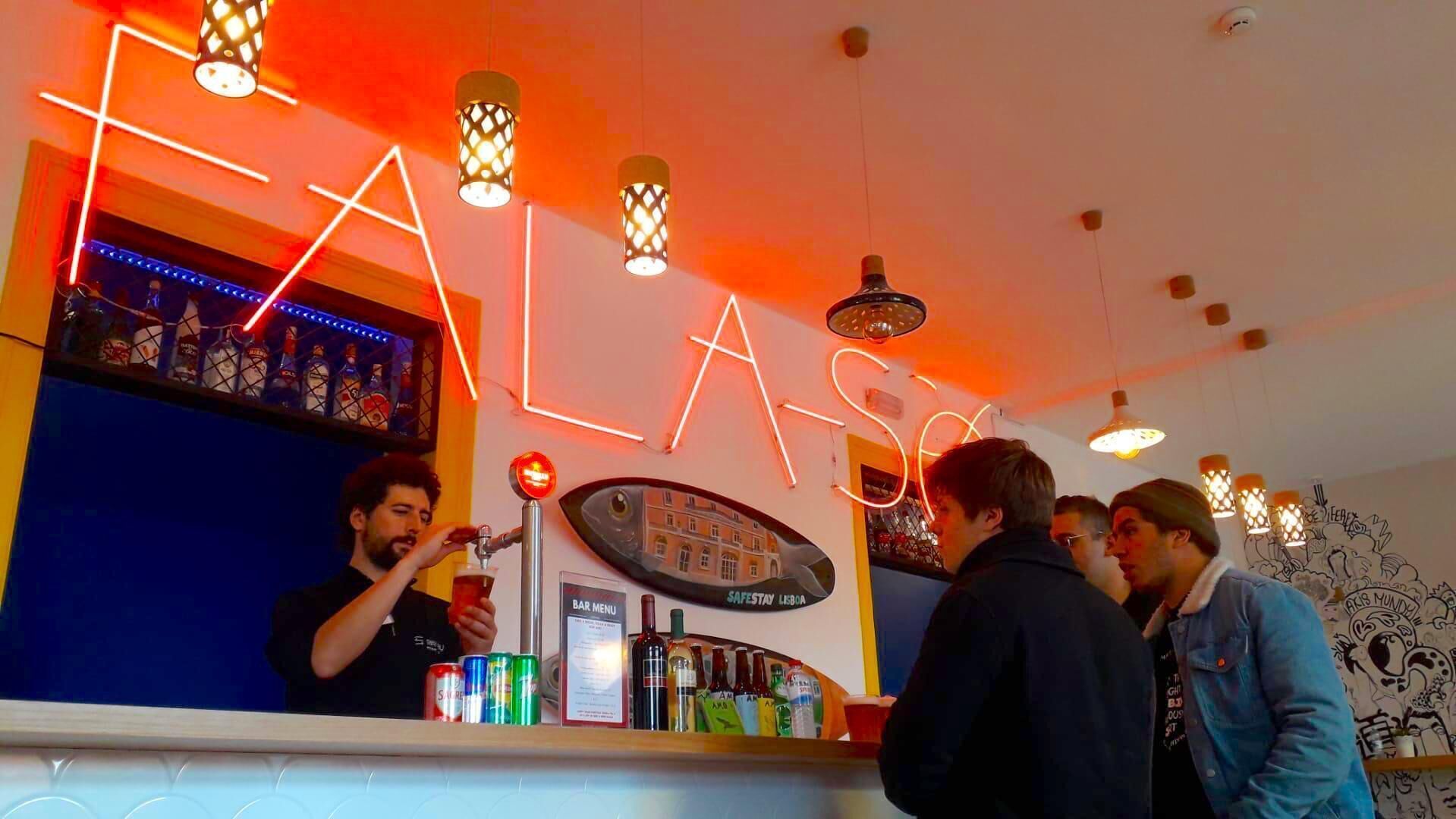 Eine Bar mit Neonreklame, auf der "ALAS" steht, und ein Barkeeper, der Getränke serviert.