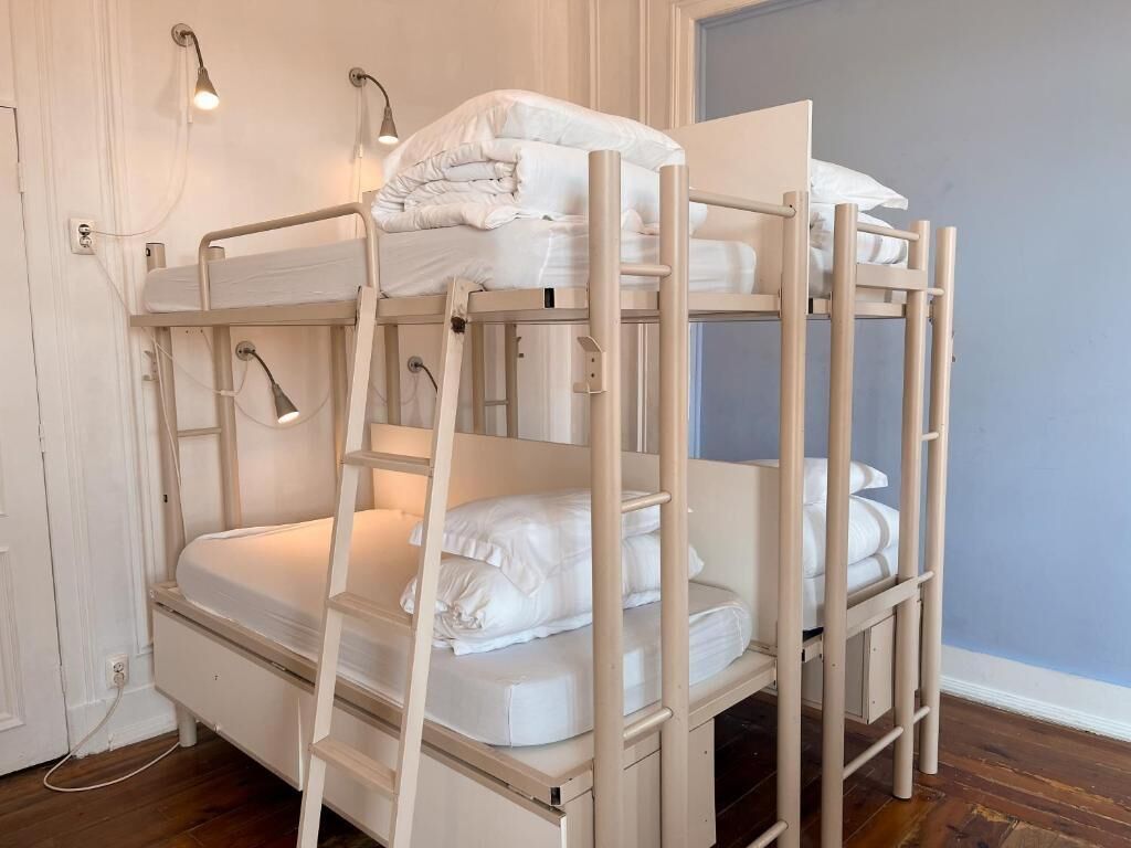 Un lit superposé à trois niveaux, chaque niveau étant équipé d’un matelas et d’oreillers. Des lampes murales sont fixées sur le côté gauche.