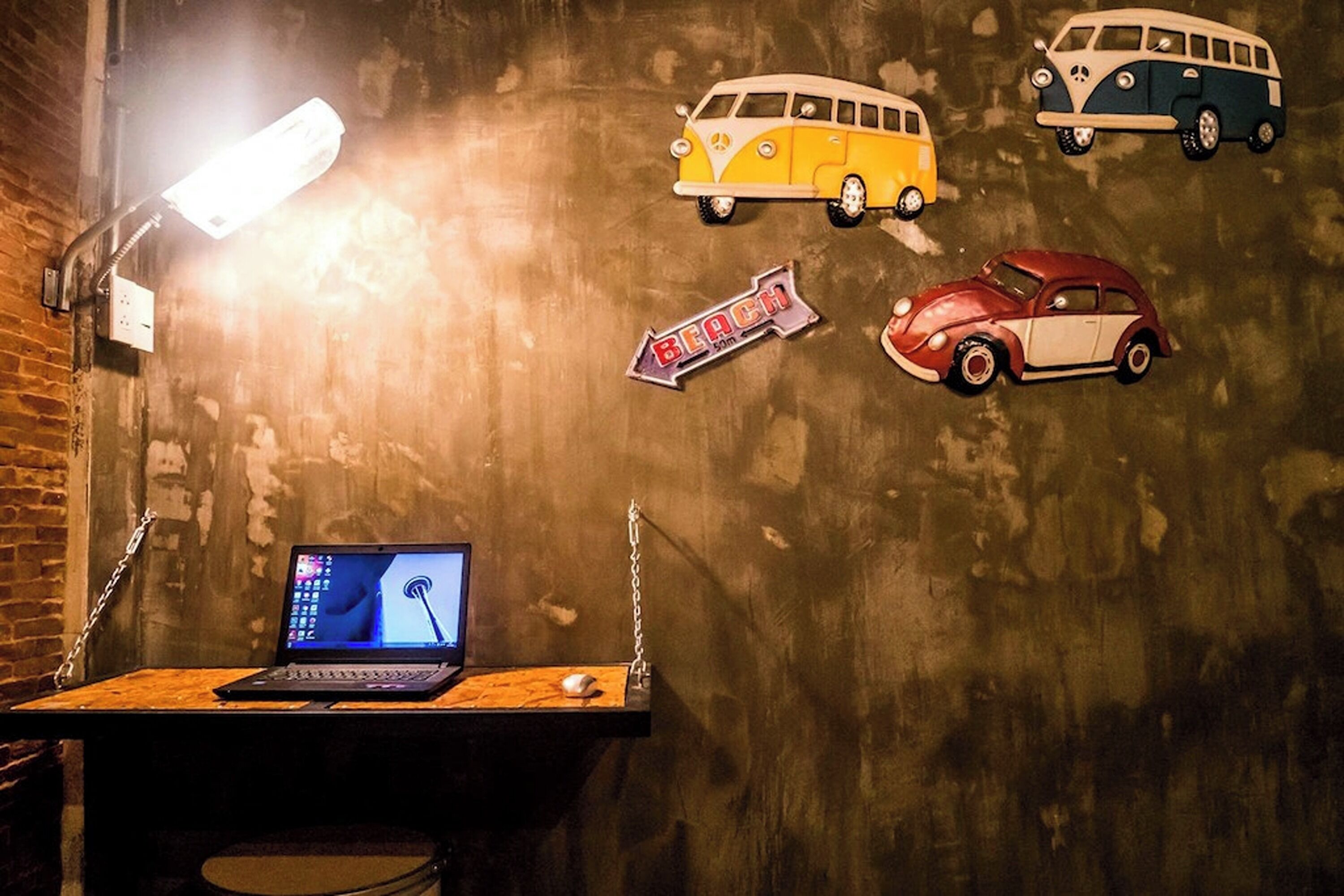 Une pièce comprenant un bureau, un ordinateur portable et un mur décoré d’autocollants représentant des voitures anciennes.