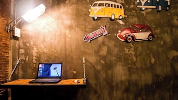 Ein Zimmer mit Schreibtisch, einem Laptop und einer Wand, die mit Vintage-Autoaufklebern verziert ist.