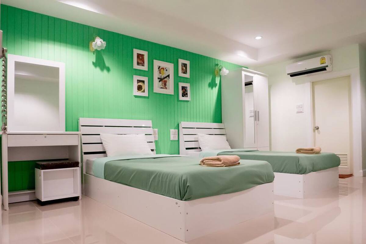 A bedroom with two beds, a wardrobe, a mirror, and a wall-mounted air conditioner.