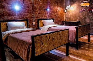 Ένα δωμάτιο με δύο κρεβάτια, έναν τοίχο από τούβλα και διακοσμητικά στοιχεία σε ρετρό στυλ, εμπνευσμένα από παλιά φορτηγά.