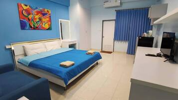 Habitación de hotel con cama, escritorio, silla, cortina azul y un cuadro colorido en la pared.