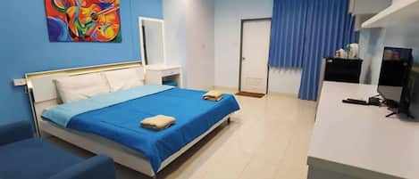 Ein Hotelzimmer mit Bett, Schreibtisch, Stuhl, einem blauen Vorhang und einem farbenfrohen Bild an der Wand.