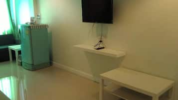 Ein Zimmer mit einem flachbildfernseher, der an einem weißen Regal befestigt ist, einem kleinen Tisch und einer Bank.