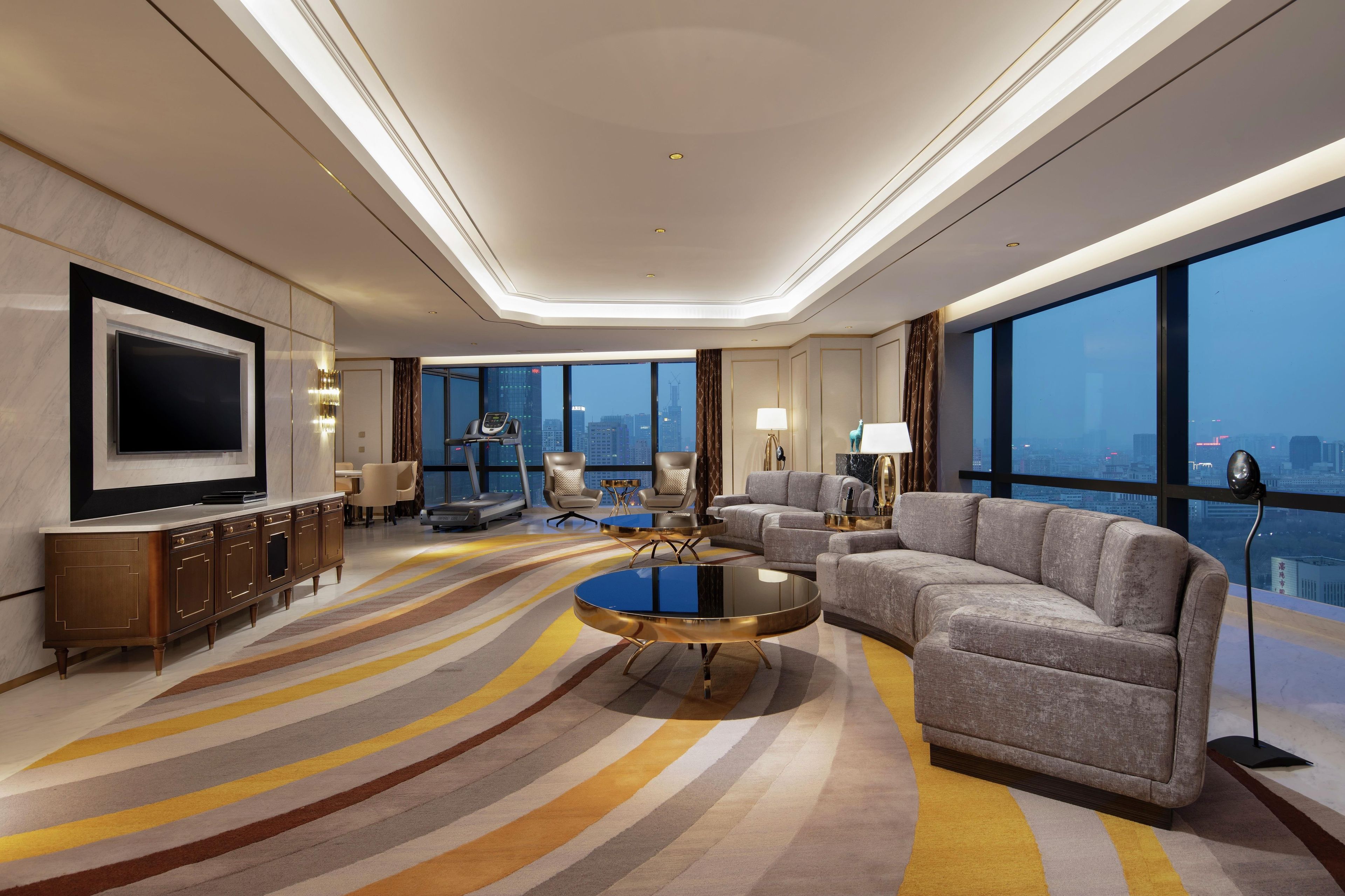 A modern hotel room with a large flat-screen TV, a sofa, a coffee table, and a view of the city skyline.