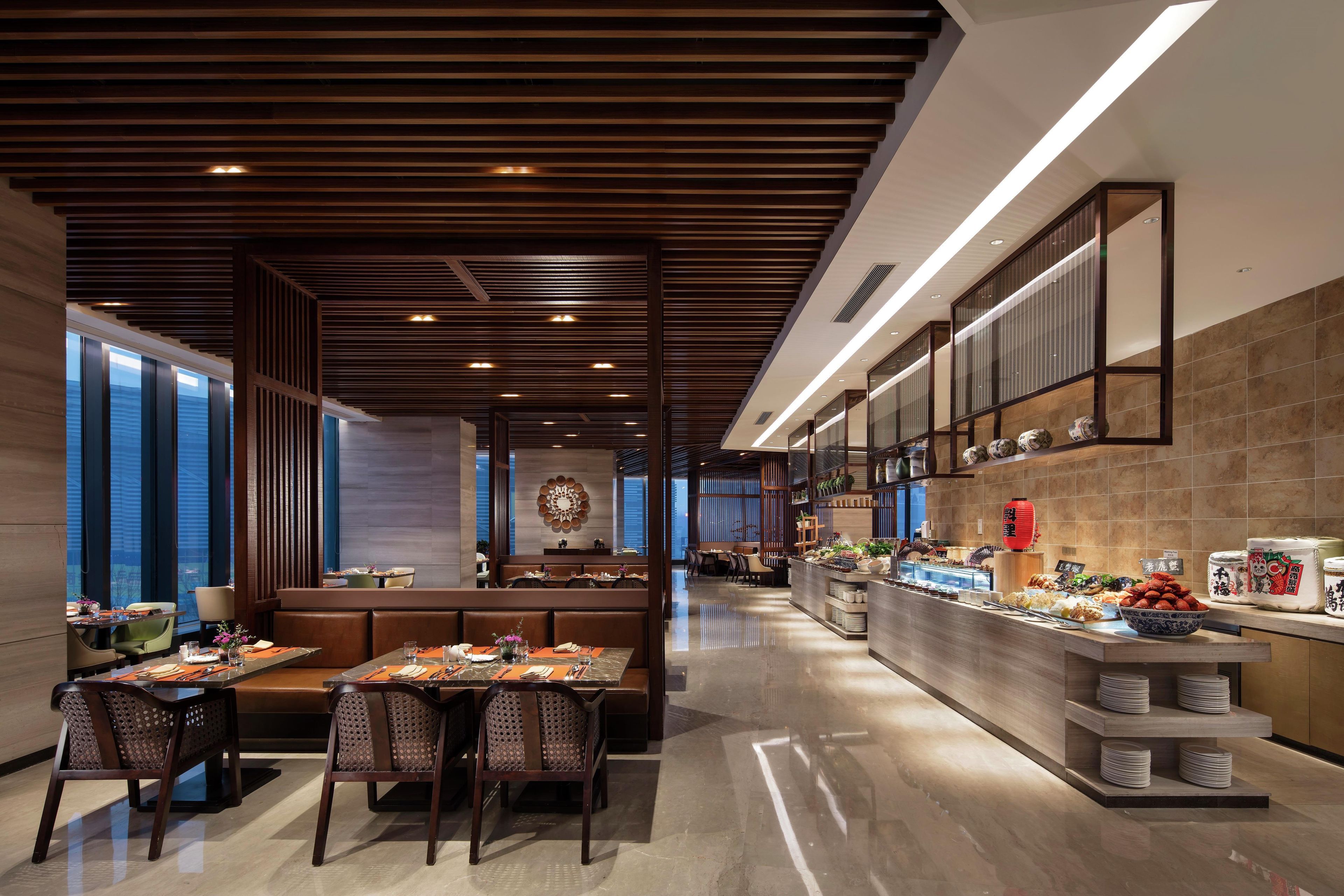 A modern restaurant interior with a central dining area, a buffet counter, and a view through large windows.
