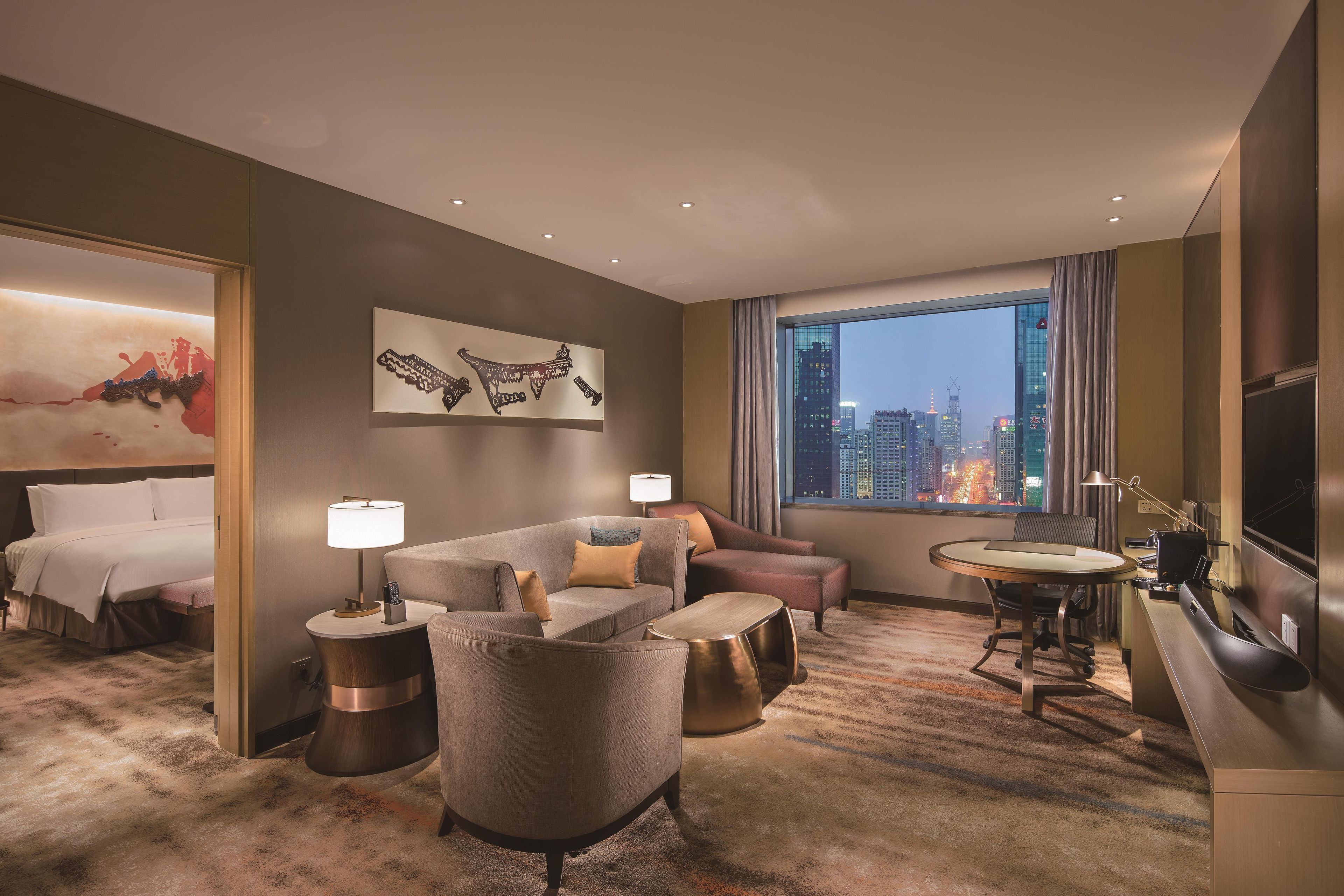 A hotel room with a bed, a sofa, a desk, and a view of the cityscape.