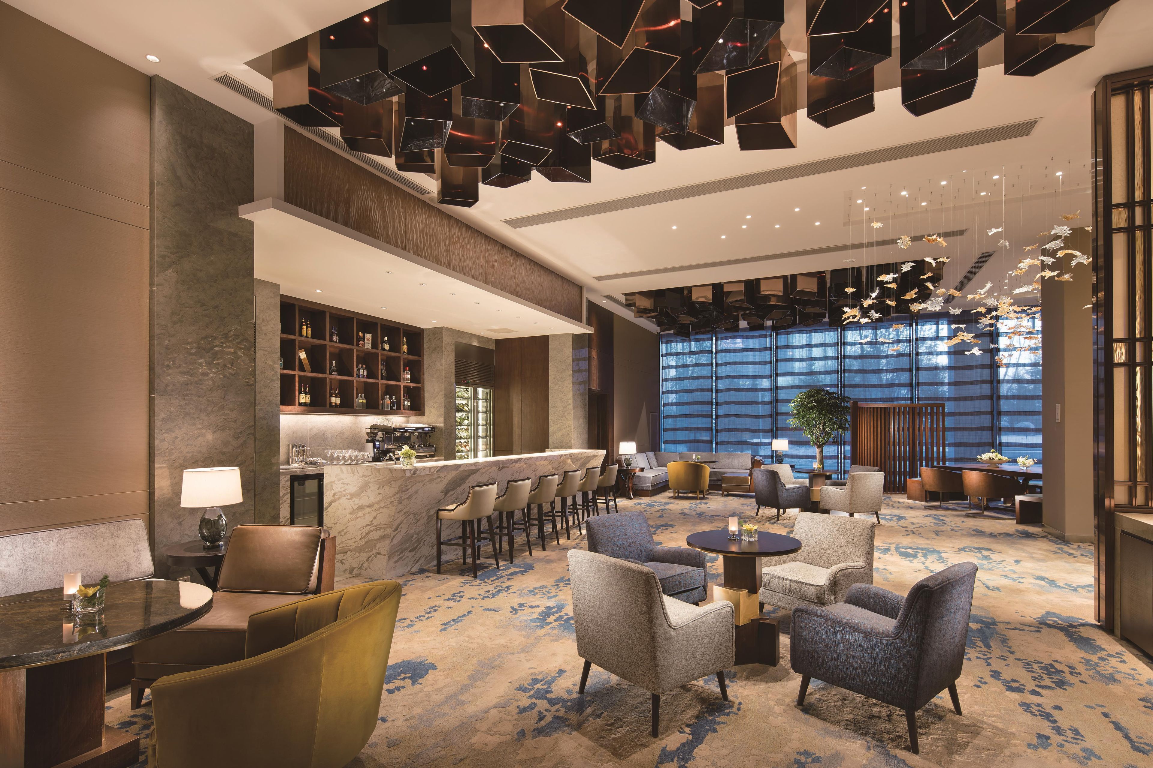 A modern hotel lobby with a bar area, seating arrangements, and a large window providing a view.