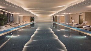 Ein modernes Hallenbad mit Liegebereichen an beiden Seiten, das durch ein elegantes Design und stimmungsvolle Beleuchtung besticht.