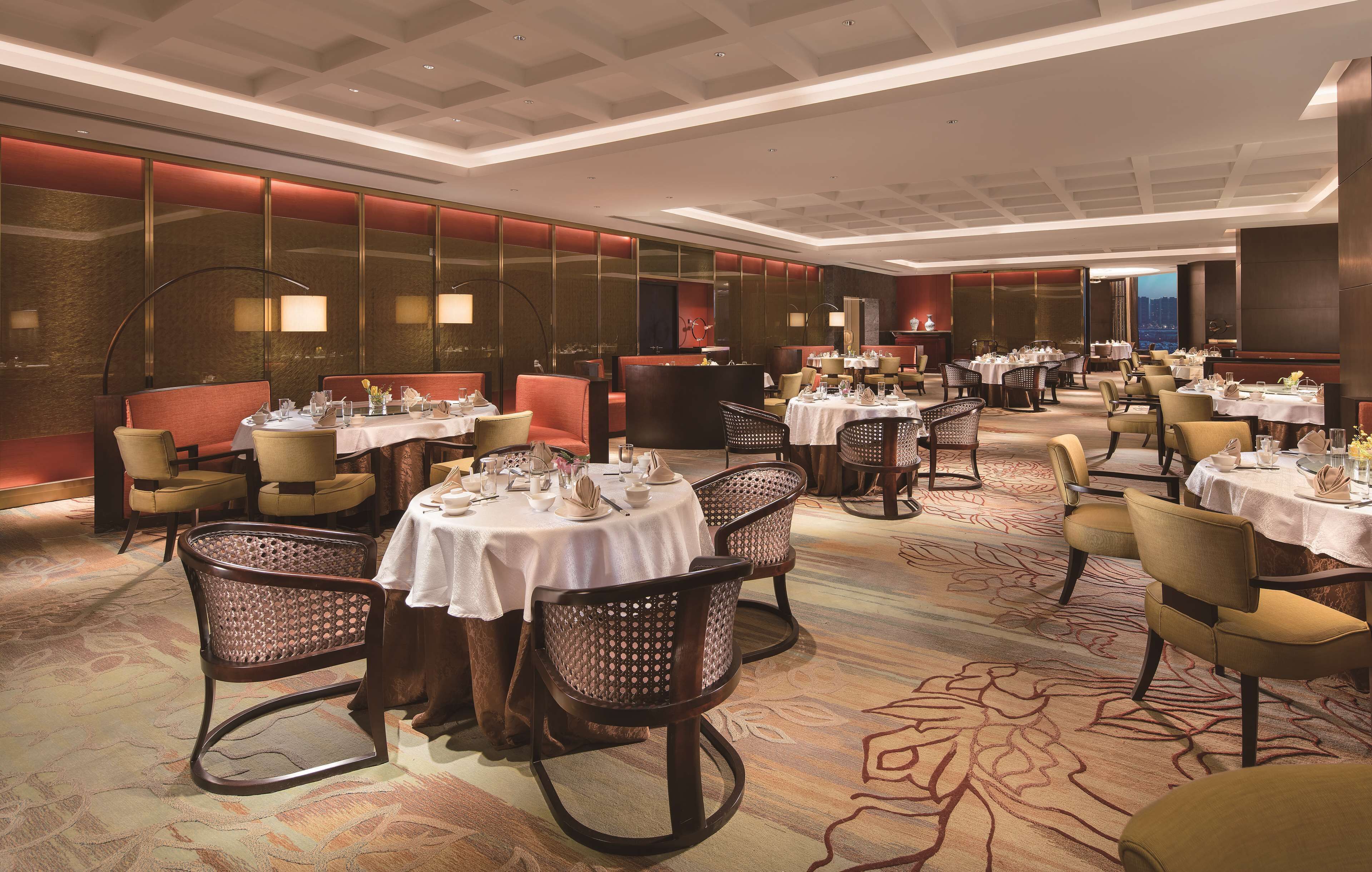 A spacious dining area with multiple tables and chairs, featuring a modern ceiling design and a carpeted floor.