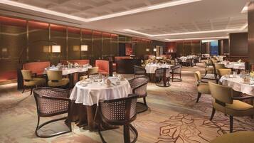 A spacious dining area with multiple tables and chairs, featuring a modern ceiling design and a carpeted floor.