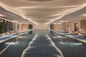 A modern indoor swimming pool with lounge areas on either side, a clear pathway down the center, and a ceiling with recessed lighting. - Hilton Shenyang (Shenyang)