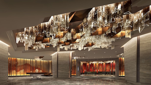 Eine geräumige Lobby mit einem modernen Kronleuchter, Marmorböden und einer Rezeption mit roter Akzentwand.