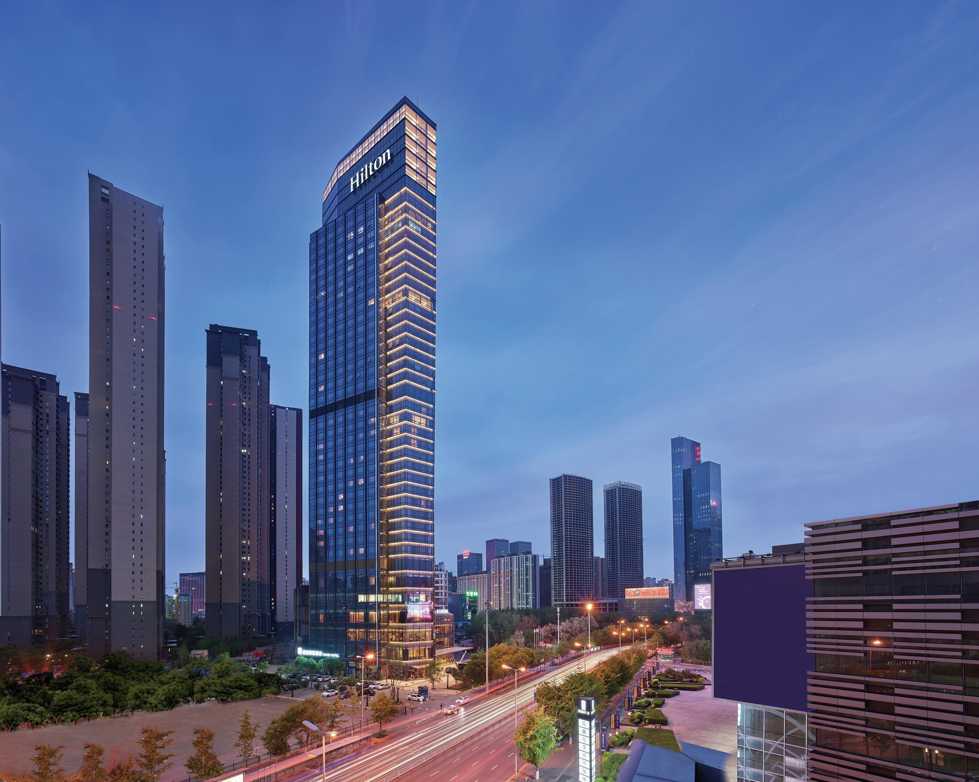 A high-rise hotel with a prominent 'Hilton' sign, surrounded by other tall buildings in a cityscape.