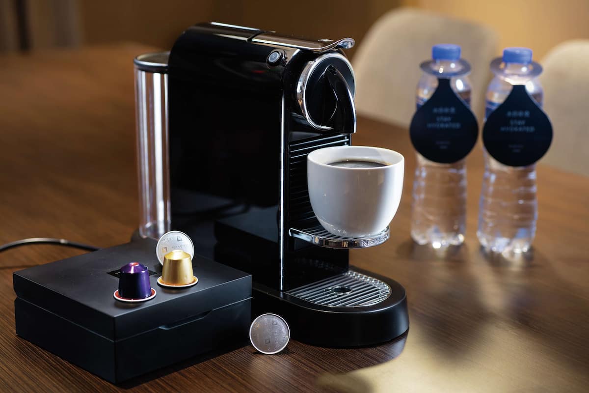 A coffee maker with a cup of coffee, two water bottles, and a small decorative item on a wooden table.