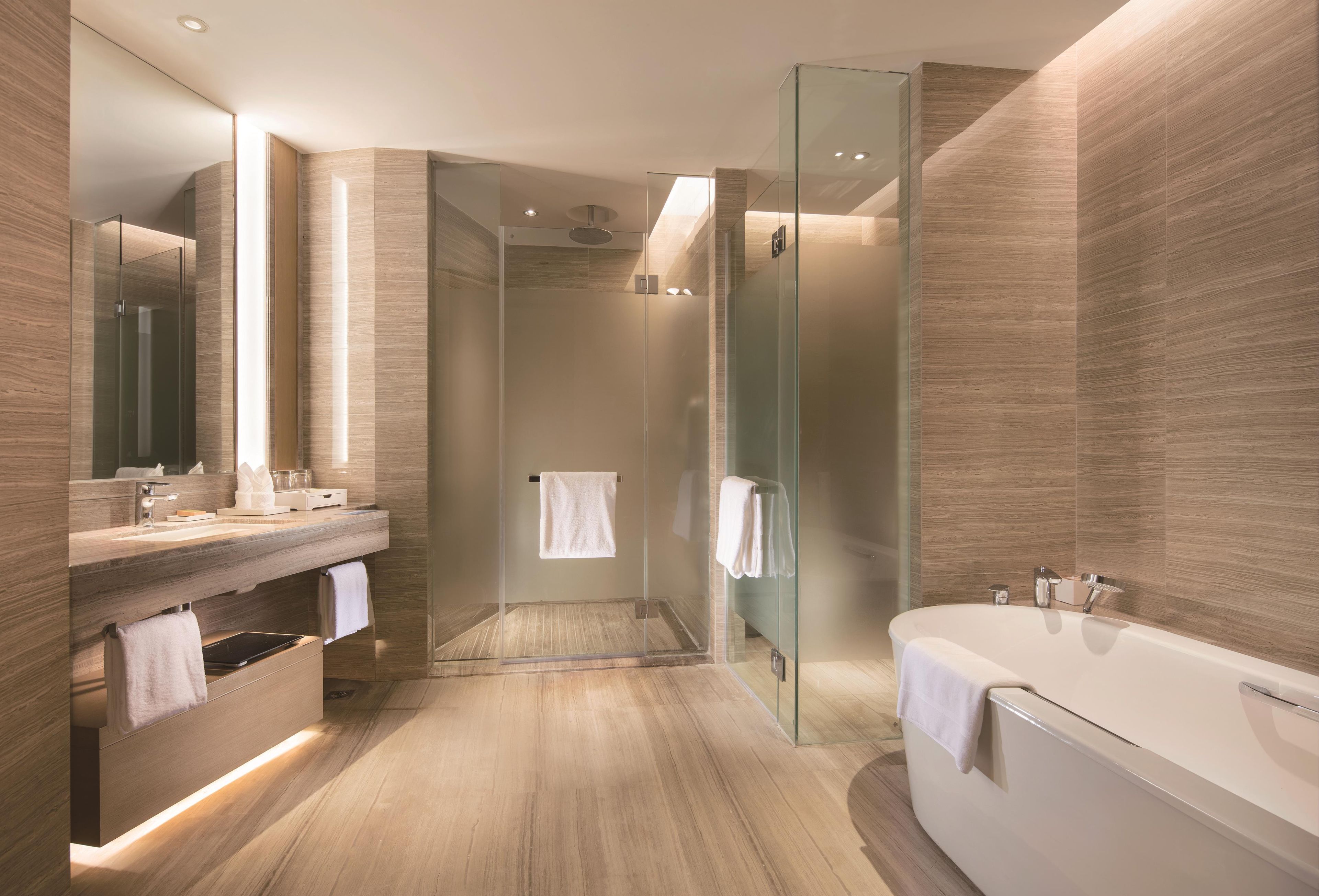 Un baño moderno con ducha envuelta en vidrio, bañera independiente y tocador con espejo.