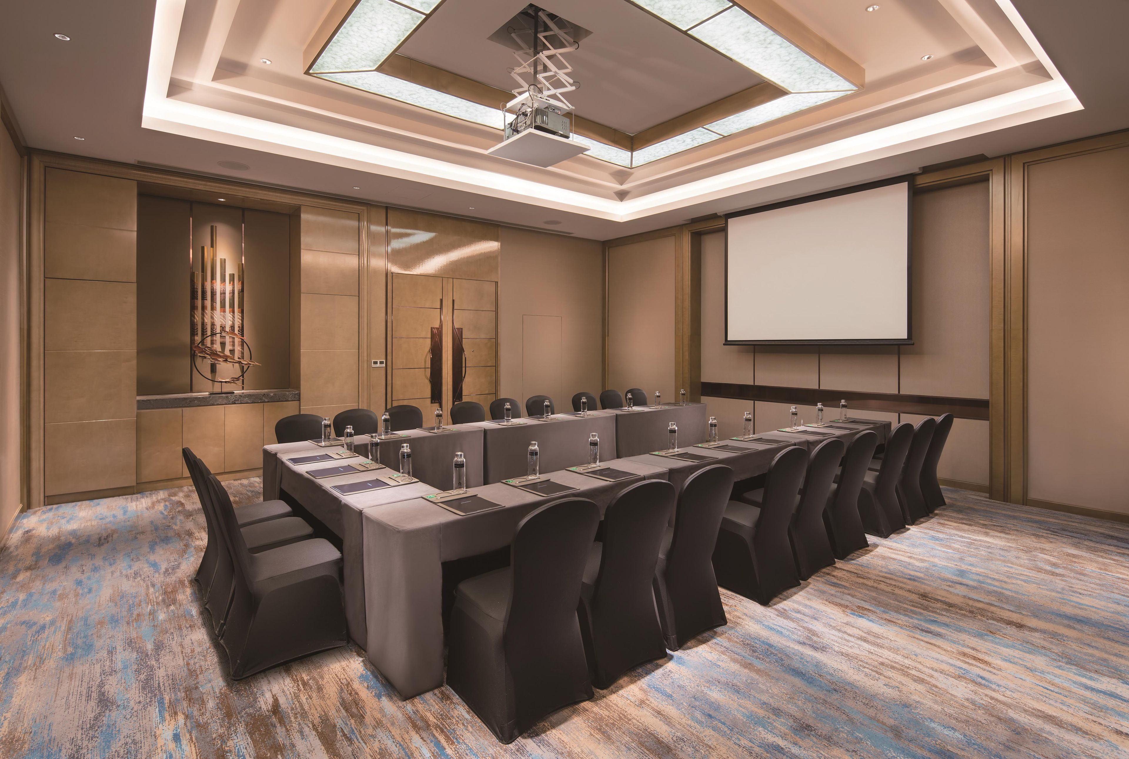 A conference room with a long table, chairs, a projector screen, and a ceiling with skylights.