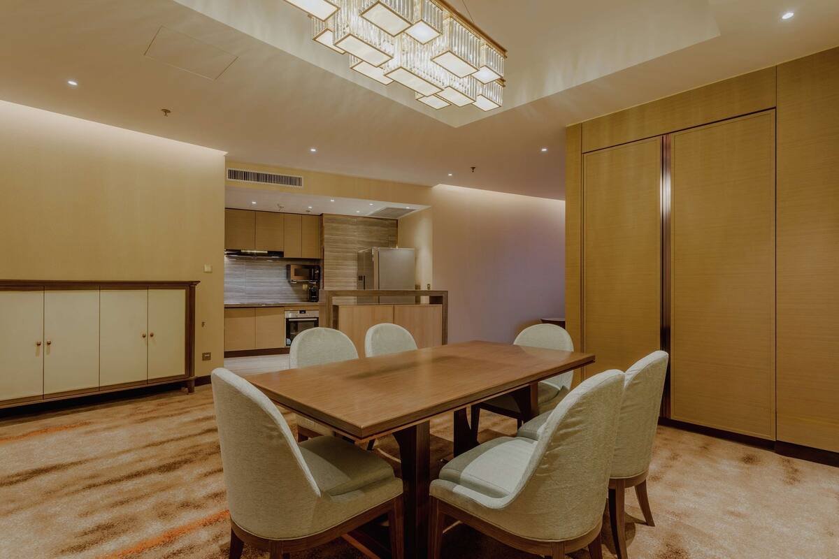 A dining area with a wooden table and six chairs, a kitchen in the background, and a large wardrobe.