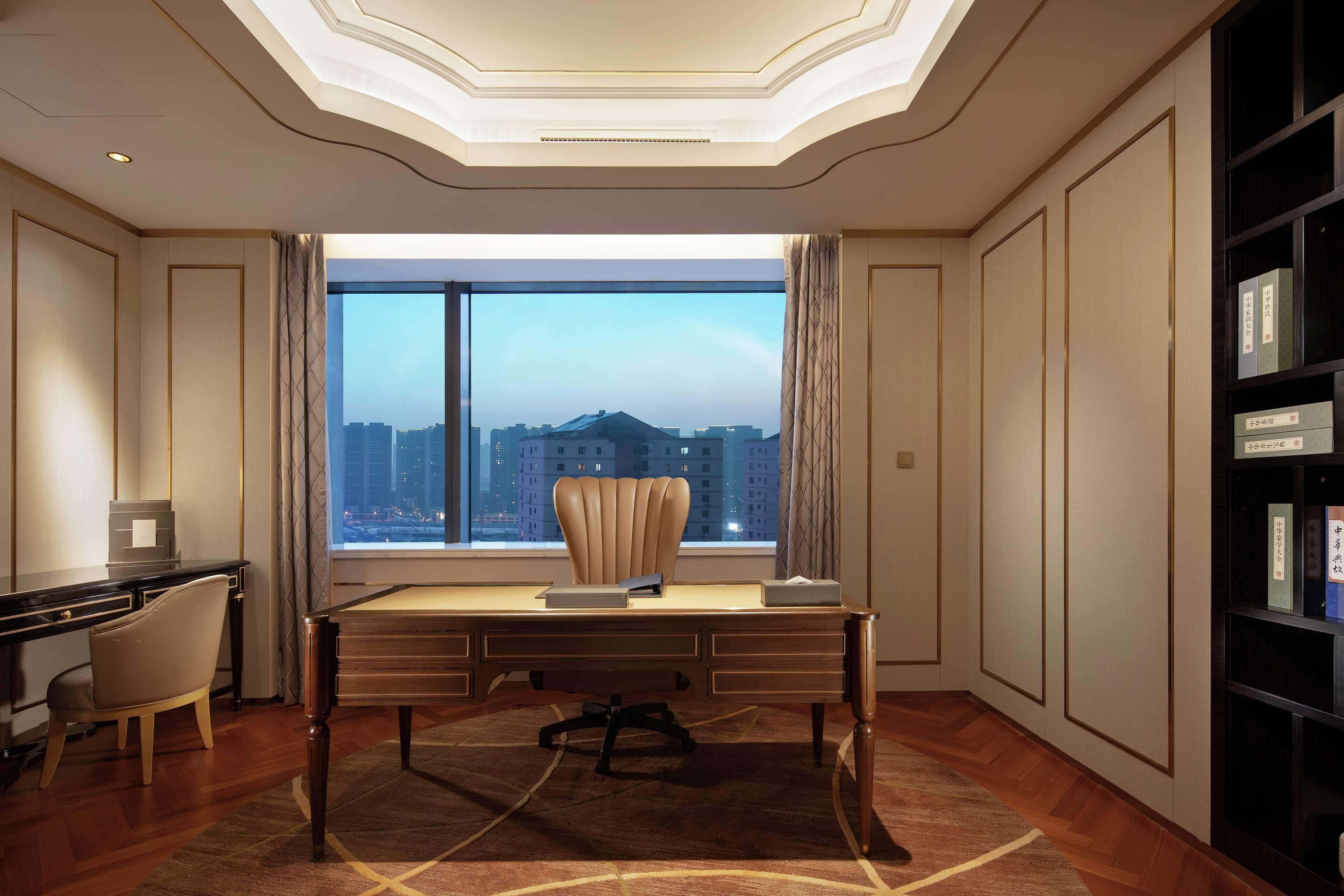 A modern hotel room with a large desk, a comfortable chair, and a view of the cityscape through a large window.
