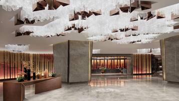 A modern lobby with a reception desk, decorative plants, and a unique hanging light fixture.
