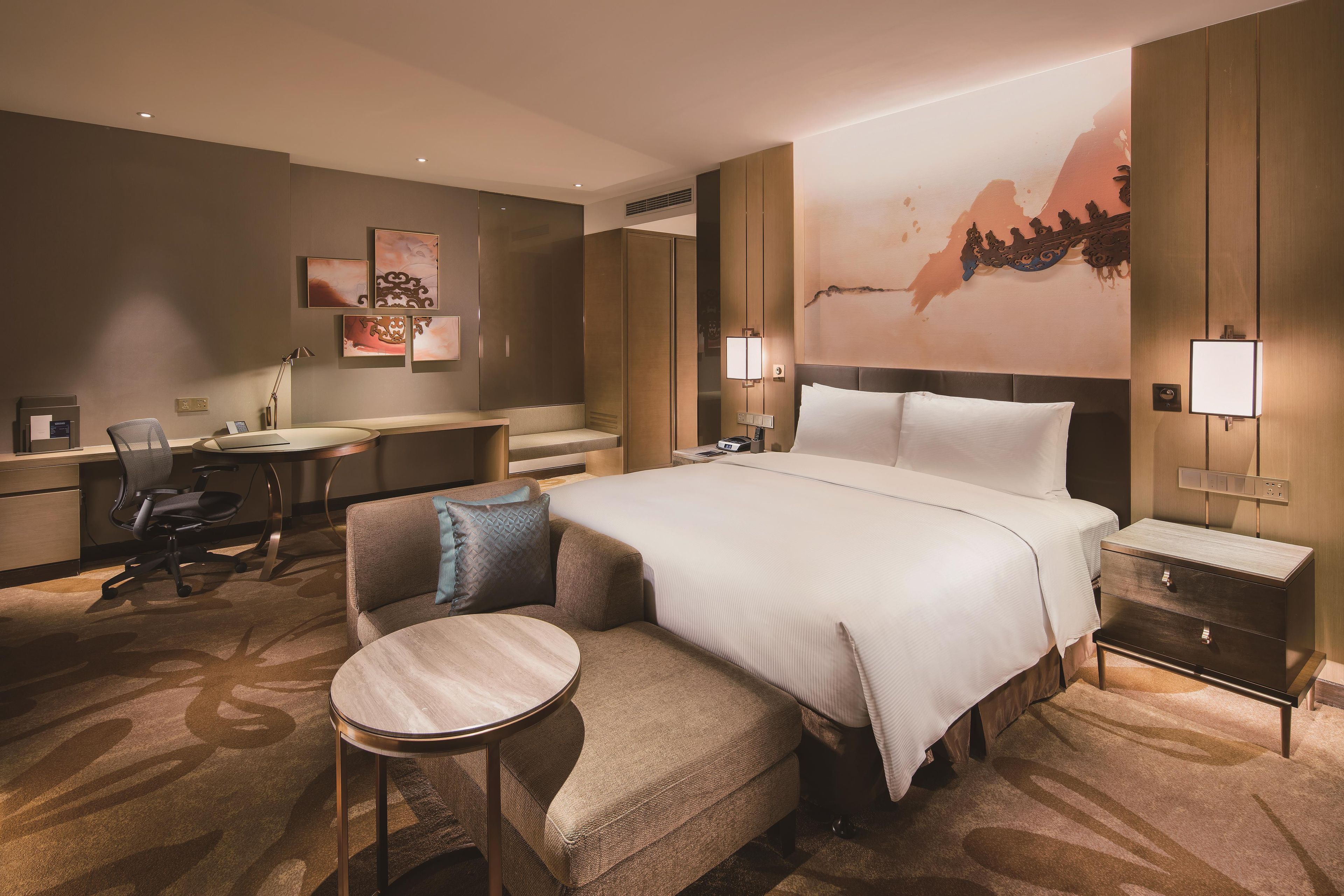 A hotel room with a bed, a desk, a chair, and a small table.