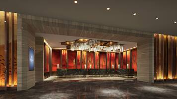 A modern hotel lobby with a marble reception desk, a large chandelier, and a red accent wall.