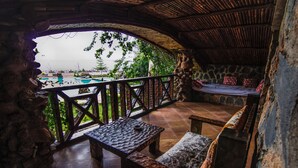 Un espacio de estar al aire libre cubierto con pared de piedra, mobiliario de madera y vista a una piscina.