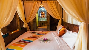 Una cama con una colcha a rayas de colores, un cojín decorativo y un arreglo floral.