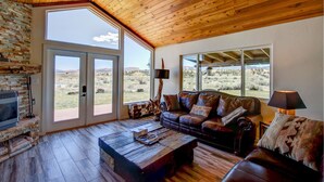 A spacious living room with a fireplace, leather sofa, and large windows offering a view of the desert landscape. - Sevier River Retreat (Hatch)