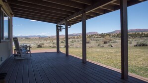 A covered outdoor area with a wooden deck, a rocking chair, and a view of a desert landscape. - Sevier River Retreat (Hatch)