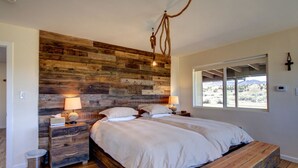 A bedroom with a wooden headboard, two bedside tables with lamps, a large bed with white bedding, and a window with a view of the outdoors. - Sevier River Retreat (Hatch)
