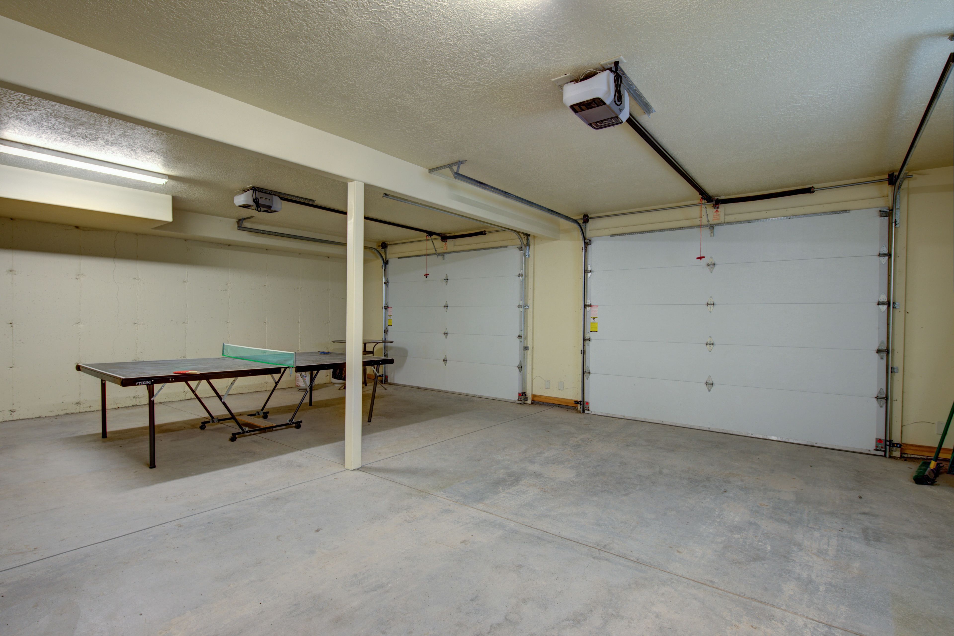 A spacious indoor area with a ping pong table, a white ceiling, and two garage doors.