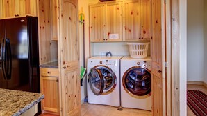 A compact kitchen with wooden cabinetry, a black refrigerator, and two front-loading washing machines. - Ridgetop Hideaway (Hatch)