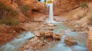 A waterfall cascading into a rocky stream surrounded by reddish-brown cliffs.