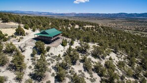 An aerial view of a lodge with a green roof, surrounded by a forested landscape and mountains in the distance. - Ridgetop Hideaway (Hatch)